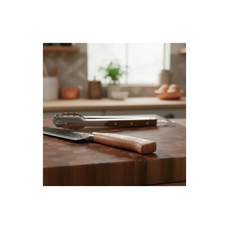 Set parrillero Kangkawe cuchillo martillado y pinza sobre tabla de madera para asado