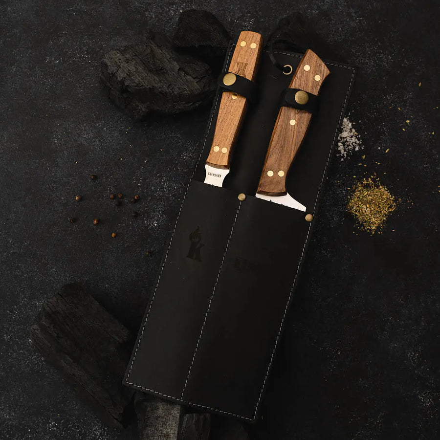 Set parrillero Kangkawe con funda de cuero negra sobre carbón de parrilla